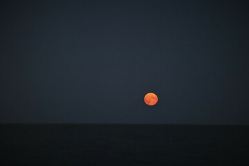 Red moon against a dark blue sky at the beach