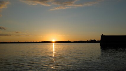 Naklejka na ściany i meble Sunset behind horizon with reflection and glitter on lake