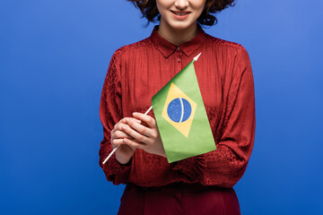 cropped view of happy language teacher smiling while holding flag of Brazil isolated on blue.