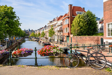 Canal lined with brick row houses on a sunny summer day. A bicycle chained to a bridge railing is...