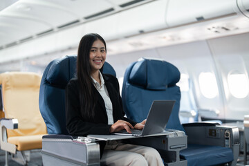 Obraz premium Female passenger sitting on plane while working on laptop computer with simulated space using on board wireless connection