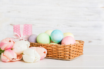 Happy Easter composition. Easter eggs in basket on colored table with yellow Tulips. Natural dyed colorful eggs background with copy space