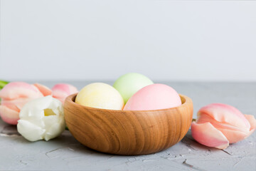 Happy Easter composition. Easter eggs in basket on colored table with yellow Tulips. Natural dyed colorful eggs background with copy space