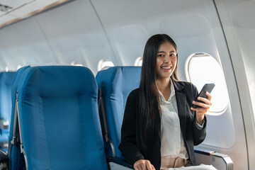 female traveler passenger sits at the window seat in economy class, using his smartphone