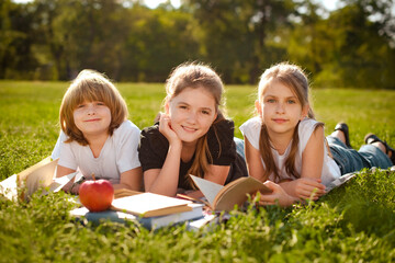 Fototapeta premium Close up of cute happy little school kids with notebooks laying in outdoor grassy park. group portrait looking at camera