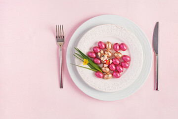 Happy Easter. Table setting for Easter holiday. Easter eggs, rabbit, flower and cutlery on pink background. Top view, flat lay
