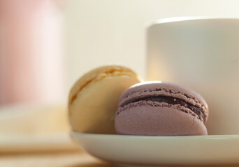 Selective focus. Macaroons are in a saucer next to a mug of tea. Yellow and purple macarons. Food, desserts. Photo taken with a Helios 44 lens. Simple composition.
