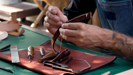 Close-up hands handmade leathermakers brown leather bag strap handle made animal skin other hand...