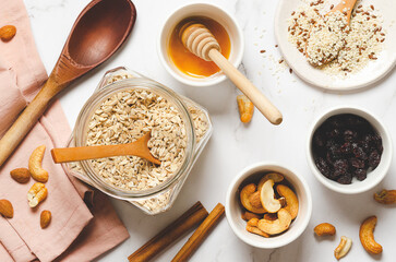 Making homemade granola. Oatmeal with nuts, seeds, cinnamon sticks and honey on a white marble background, top view.