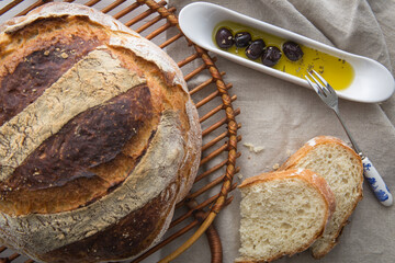 Close up of freshly baked round artisan bread with black olives in olive oil with oregano and a...
