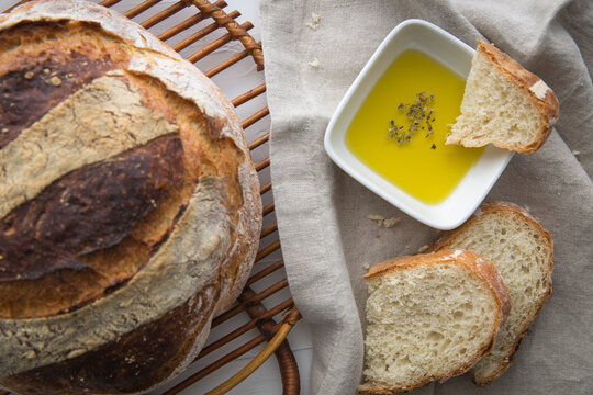 Close up of freshly baked round artisan bread, olive oil with oregano on the side which a piece pf bread dipped in.