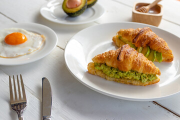 Croissant sandwich with egg,avocado on white dish and honey, coffee. breakfast and healthy food concept