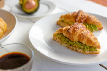Croissant sandwich with egg,avocado on white dish and honey, coffee. breakfast and healthy food concept.