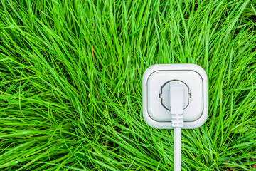 Weisse Steckdose mit Stromstecker und Kabel auf grünem Gras