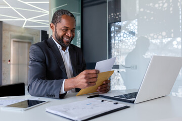 African american businessman reading good news, man inside office workplace holding mail envelope...