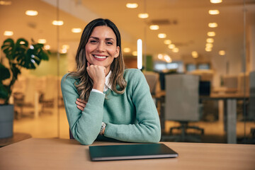 Portrait of a smiling female employee, sitting at the office, elegantly dressed.