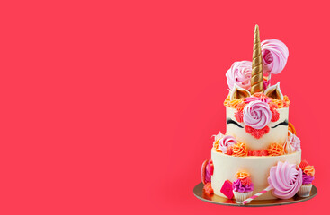 Tall and bright unicorn cake with chocolate, meringue swirls and cupcakes. Isolated on pink background with copy space on a side. Horizontal