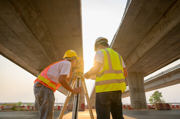 A team of male survey engineers using a theodolite in the construction of a motorway bridge.