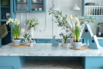Stylish cuisine with flowers in vase. Wooden kitchen in easter decor. Cozy home decor. Kitchen utensils, dishes and plate on table. kitchen island in dining room. Blue kitchen interior with furniture