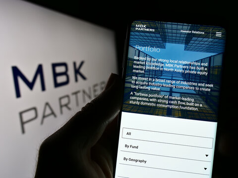 Stuttgart, Germany - 03-22-2023: Person holding cellphone with webpage of Korean investment company MBK Partners Ltd. on screen in front of logo. Focus on center of phone display.