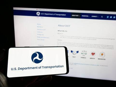 Stuttgart, Germany - 03-22-2023: Person holding cellphone with logo of United States Department of Transportation (USDOT) on screen in front of web page. Focus on phone display.