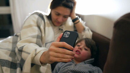 Mother holding phone for child to speak with family member on video conference. Family lifestyle moment of little boy in virtual conversation using smartphone