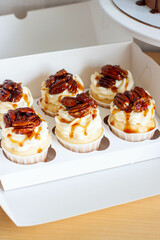 Close up on a set of cupcakes decorated with pecan nuts and maple syrup on gift box