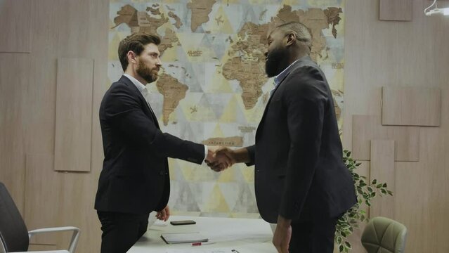 Two multiethnic big businessmen shaking hands in the office against the backdrop of the world map. Successful transaction of large transcontinental corporations. African and European businessmen.