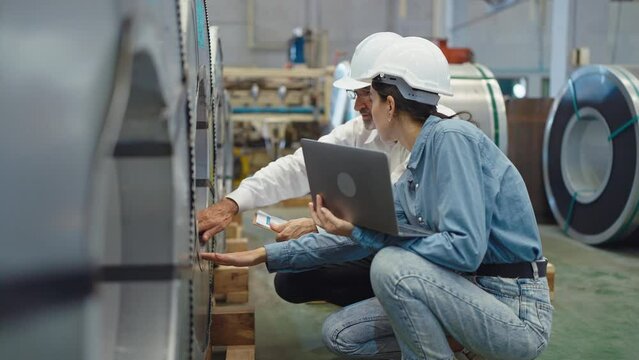 Two engineer manager leader and woman assistant holding laptop wearing helmet sitting at manufacturing factory discussing and explaining detail talking and checking production in workplace area