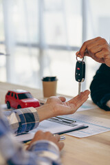 Explain promotions and car insurance for rental or purchase. A car dealer or sales manager hands the keys to the car owner and explains the terms of the car contract at a desk in the office.
