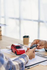 Explain promotions and car insurance for rental or purchase. A car dealer or sales manager hands the keys to the car owner and explains the terms of the car contract at a desk in the office.