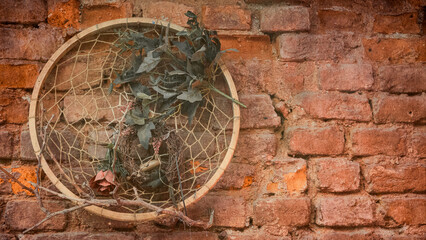 Fototapeta na wymiar The macrame wall circle with rose petals and branches is hung on a brick wall as an ornament. vintage wallpaper