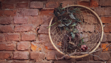 Fototapeta na wymiar The macrame wall circle with rose petals and branches is hung on a brick wall as an ornament. vintage wallpaper