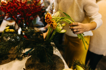 Woman working at a flower shop, making a bouquet of small orange tulips. Floral workshop concept.