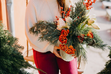 Woman holding a christmas bouquet made of red tulips, ilex berries, pine branches and amaryllis...