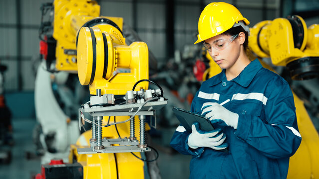 Caucasian mechatronics engineer is inspecting a lot of robotic arms in warehouse before being used in factory. A female industrial worker is using a tablet to record the results of examining machines.