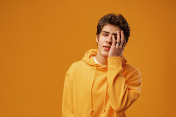 Young man wearing casual yellow hoody puts hand on face facepalm mistaken on yellow background
