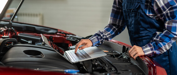 Fototapeta na wymiar Woman auto mechanic doing engine diagnostics using laptop. 
