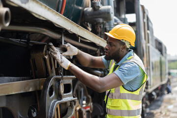 Male engineer maintenance locomotive engine, wearing safety uniform, helmet and gloves in locomotive repair garage. Male railway engineer use wrench repair train wheel in train garage