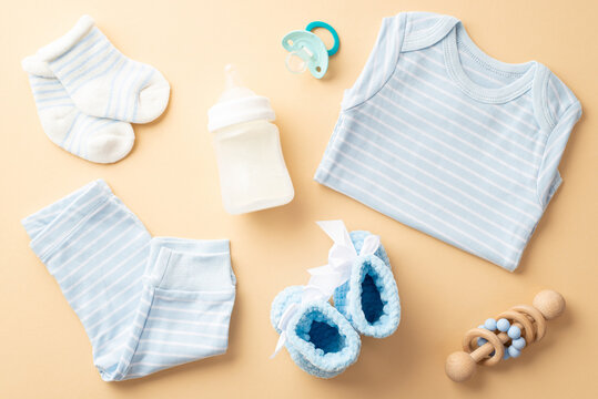 Baby accessories concept. Top view photo of blue shirt panties knitted booties socks milk bottle soother and wooden rattle on isolated pastel beige background