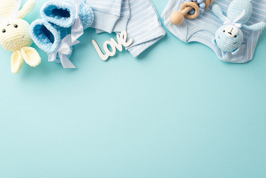 Baby accessories concept. Top view photo of infant clothes blue shirt pants inscription love knitted booties wooden rattle teddy bear and bunny toys on isolated pastel blue background with empty space