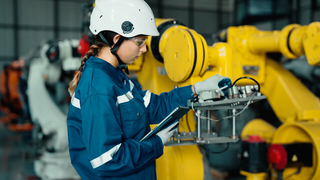 Caucasian mechatronics engineer is using a tablet to record the results of examining a lot of robotic arms. A female industrial worker with responsibility for quality checking machines in the factory.
