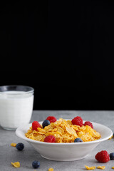 Tasty corn flakes garnished with raspberries and blueberries on a gray table. Black background, free space for text.