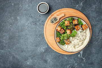 Vegan tofu poke bowl with rice and broccoli on a dark background. Clean eating, dieting, vegan food concept. top view