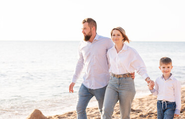 Front view family in white shirts and jeans walking on sandy tropical beach. Father, mother and son spend the weekend together. Concept: tourism vacation relax 