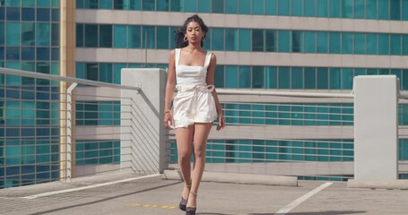 Young girl in heels walking confidently on a rooftop with city buildings in the background - Powered by Adobe