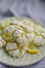 Delicious citrusy lemony snack, crunchy cracked lemon crinkle cookies coated with powdered sugar on white plate close up selective focus 