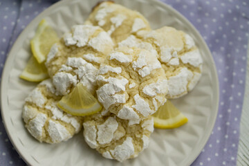Delicious citrusy lemony snack, crunchy cracked lemon crinkle cookies coated with powdered sugar on white plate close up selective focus 