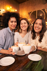 Vertical group of cheerful female friends take selfie toasting cups of cafe in coffee shop. Smiling...