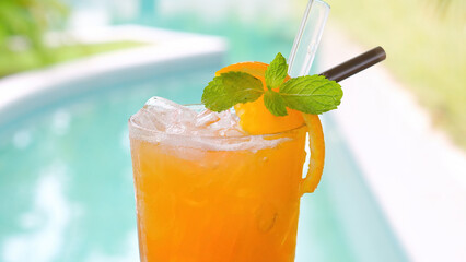 Close-up of refreshing orange drink with ice and mint leaf by the swimming pool at luxury resort spa. Healthy summer beverage to enjoy on vacation.